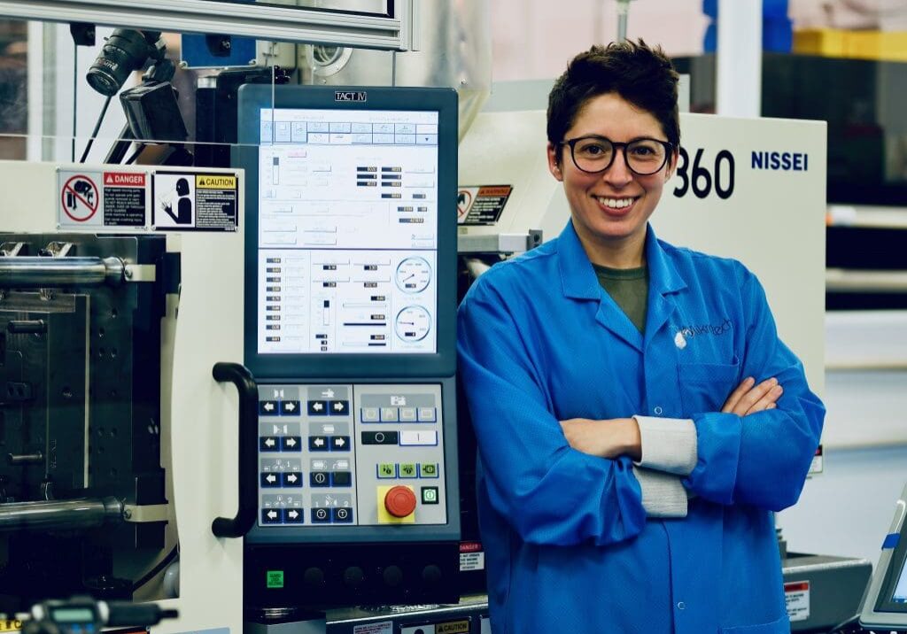 A woman in blue lab coat standing next to machine.